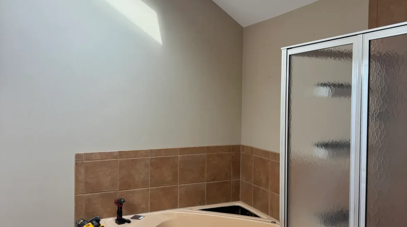 Bathroom before photo, Mokena IL - corner tub set into beige tile next to a framed obscure-glass shower enclosure