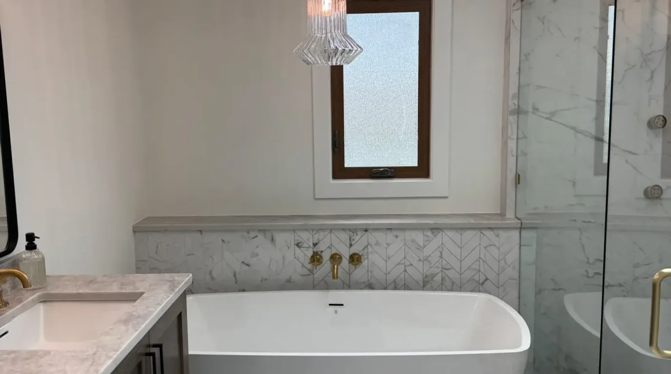 After: a freestanding soaking tub against a marble-look wall with a brass floor-standing filler, fluted glass pendant and a frameless glass shower alongside, Mokena IL
