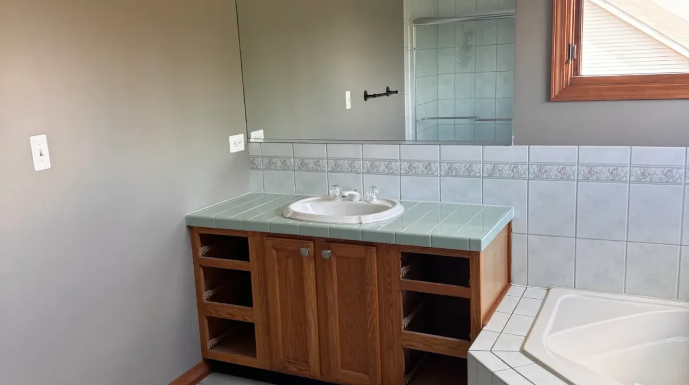 Before: an oak bathroom vanity with a seafoam-green tile countertop, drop-in sink and plate mirror in a Shorewood, IL home