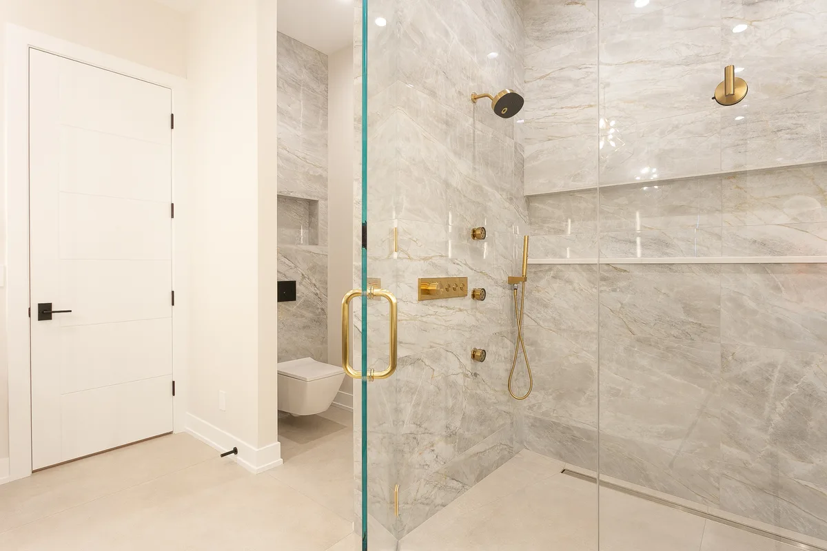 Walk-in marble shower with brass thermostatic controls, a brass handshower and a frameless glass enclosure - Lemont IL