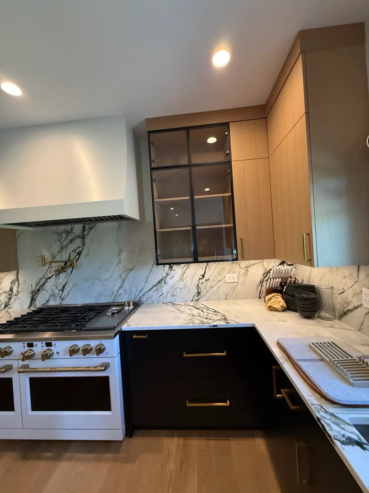 Full-height book-matched marble slab backsplash behind a brass-trimmed range, with a brass pot filler and white oak cabinetry - Mokena IL