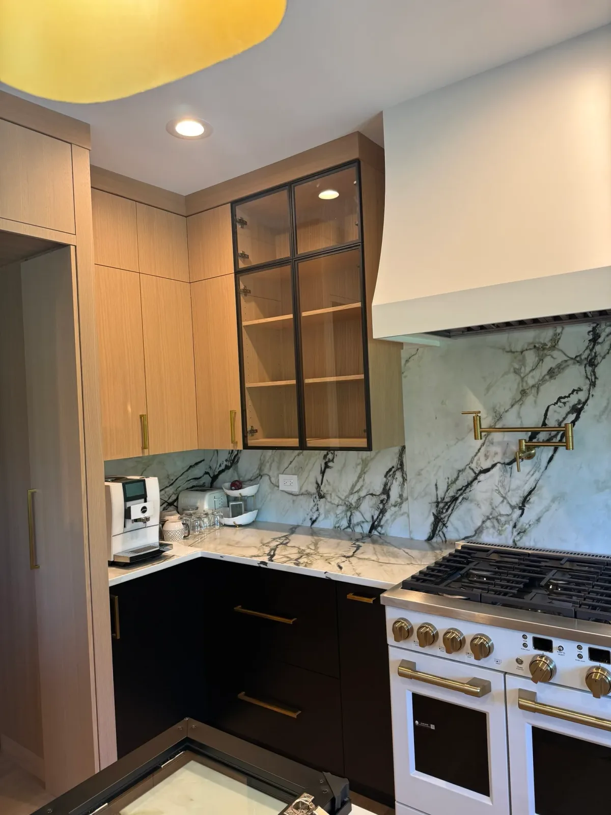 Range wall with a plaster hood, glass-front upper cabinets in a dark steel frame, marble counters and a brass pot filler - Mokena IL