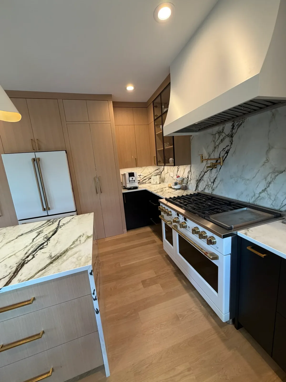 White oak kitchen with black base cabinetry, a marble slab backsplash and a professional range under a plaster hood - Mokena IL