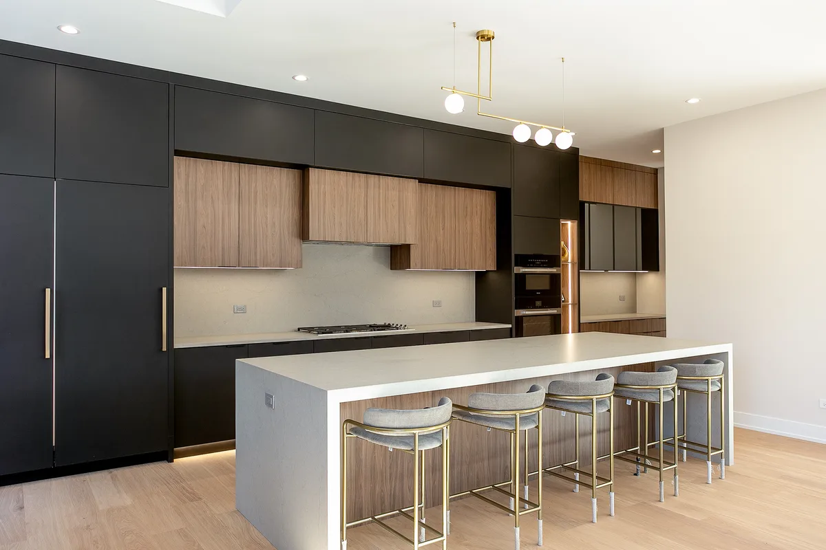 Open-plan custom kitchen with a white quartz island seating five on brass stools, walnut uppers in a matte black surround and pale oak flooring - Lemont IL