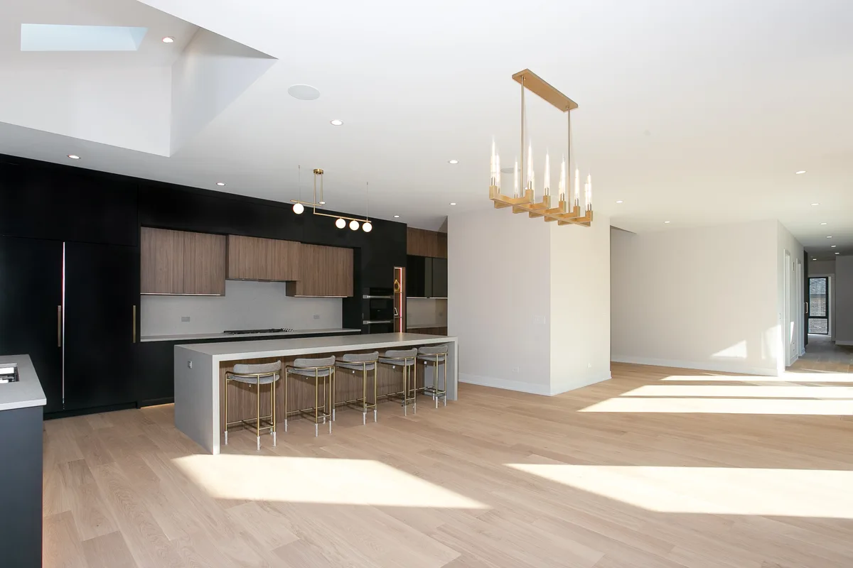 Kitchen island with seating under a linear brass chandelier, opening to the dining area with pale oak plank flooring - Lemont IL