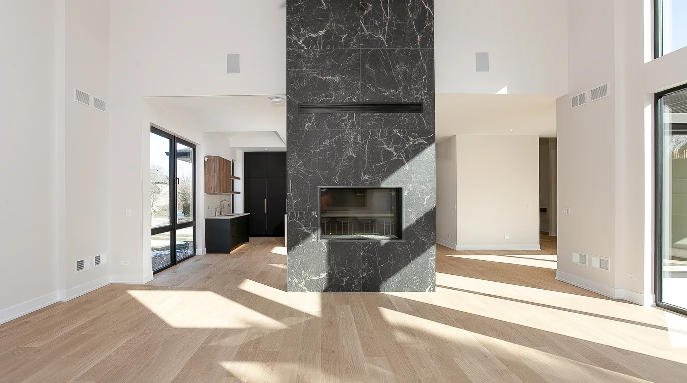 Luxe Development great room interior with a charcoal stone-look tile fireplace, pale oak floors and a double-height ceiling