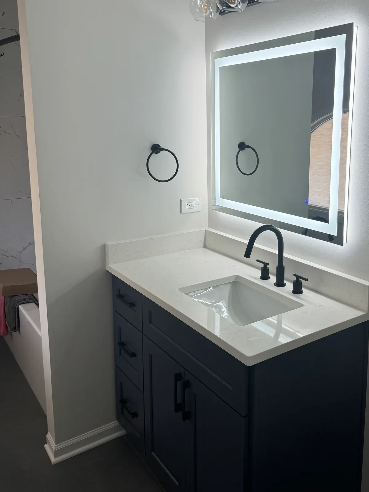 Guest bathroom navy shaker vanity with a white quartz top, a rectangular undermount basin, matte-black tapware and a backlit mirror under a four-globe fixture - Shorewood IL