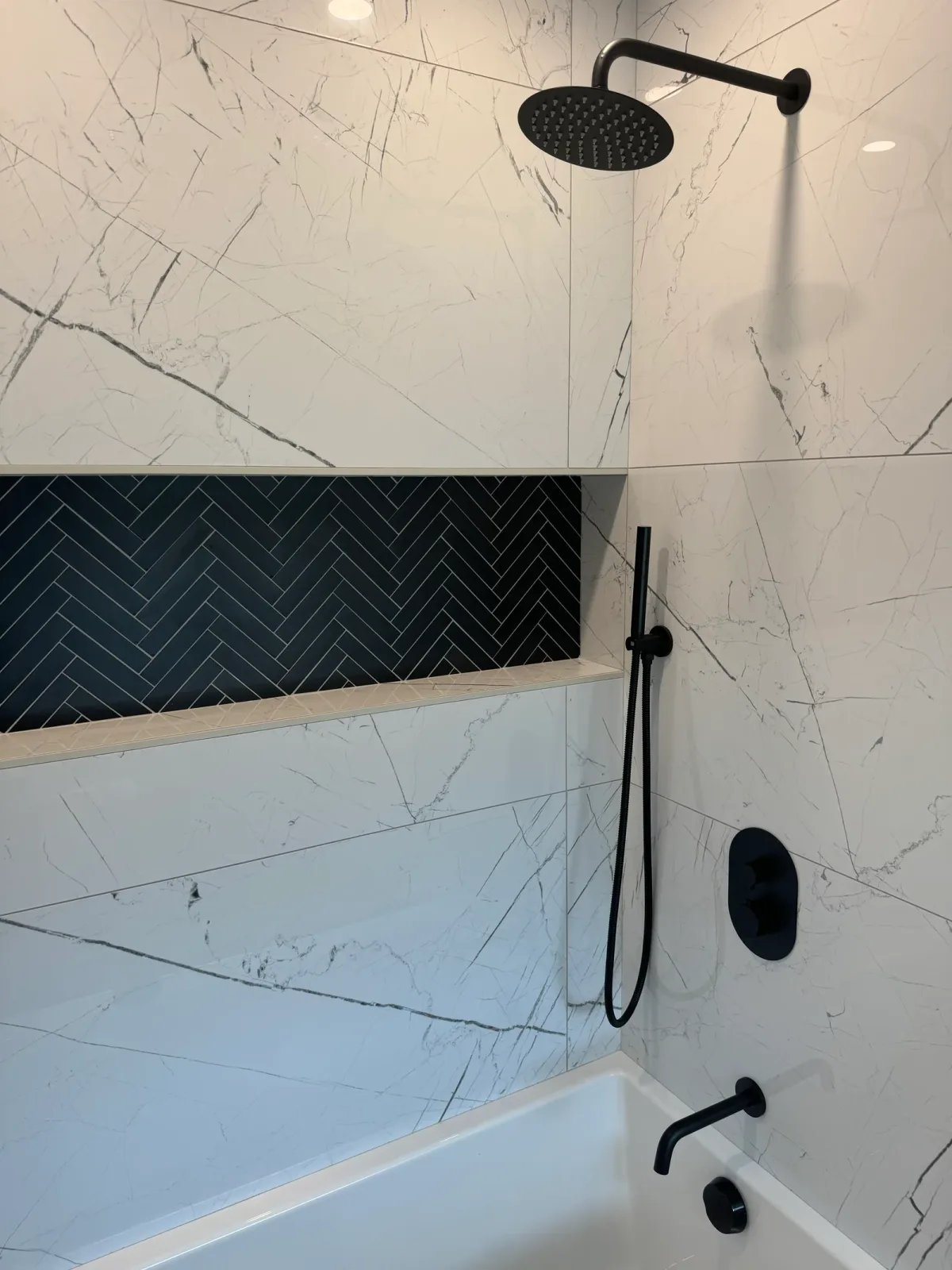 Black herringbone niche and matte-black fittings against large-format white marble-look porcelain above the guest tub - Shorewood, IL