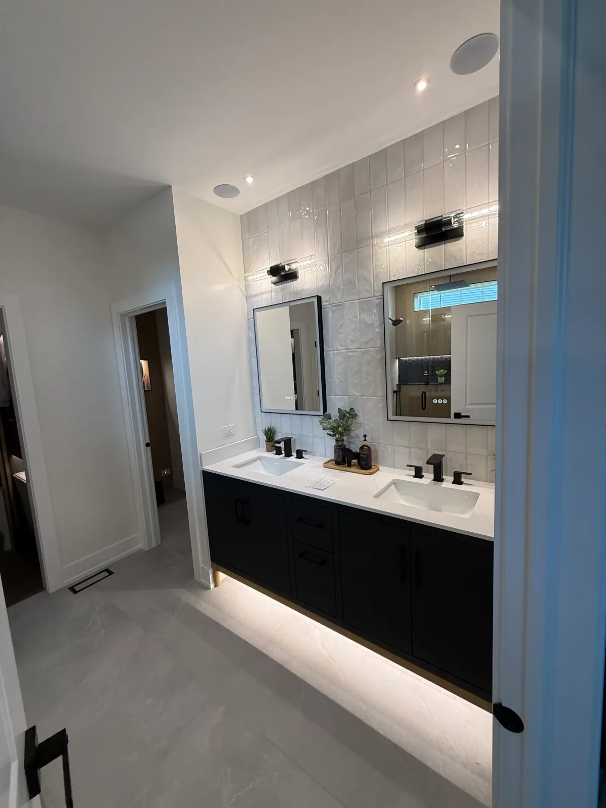 Bathroom remodel after photo by bathroom remodeling contractors in Shorewood, IL - black flat-panel double vanity with a white stone-look counter, two rectangular undermount basins, matte black tapware and two black-framed backlit mirrors on glossy white stacked tile