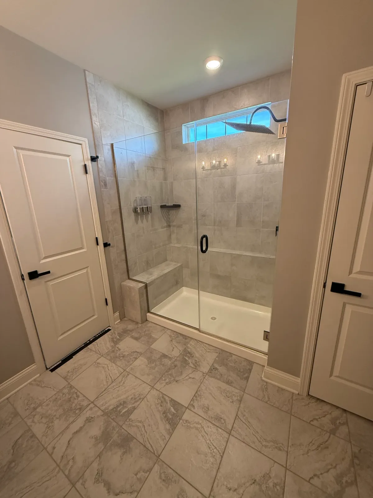 Bathroom before photo, Shorewood IL - alcove shower in beige stone-look tile with a built-in tiled bench, a one-piece white pan and glass panels in slim metal channels, with cream marble-look floor tile laid on the diagonal