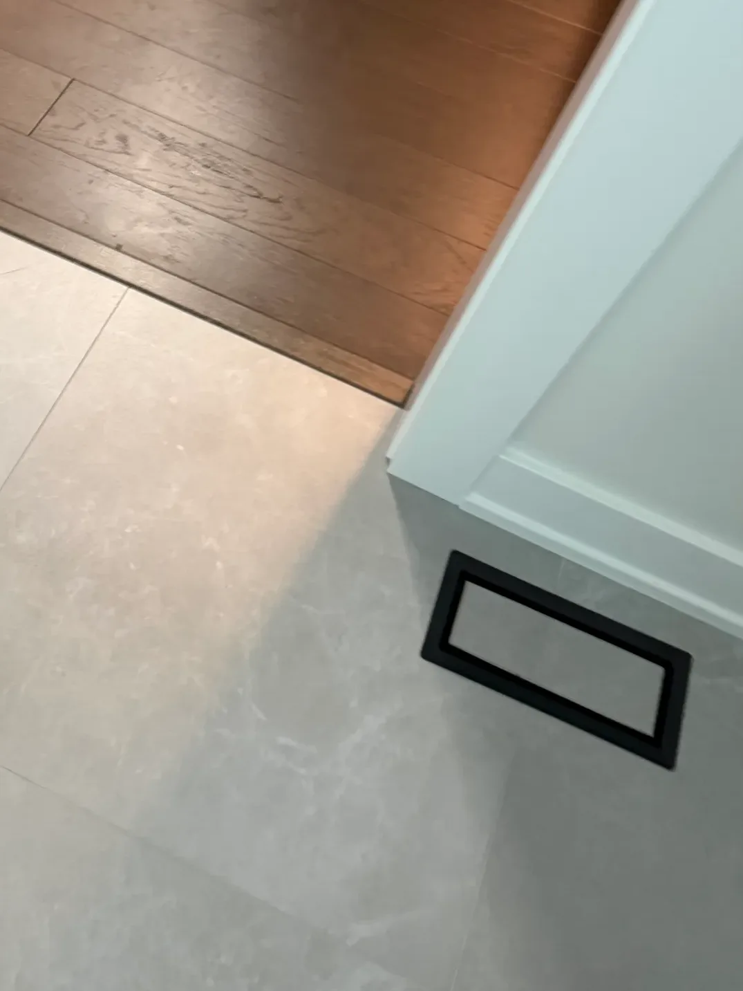 Bathroom remodel after photo, Shorewood IL - new large-format grey stone-look floor tile meeting a stained wood floor at a flush threshold, with a black linear floor register set into the tile
