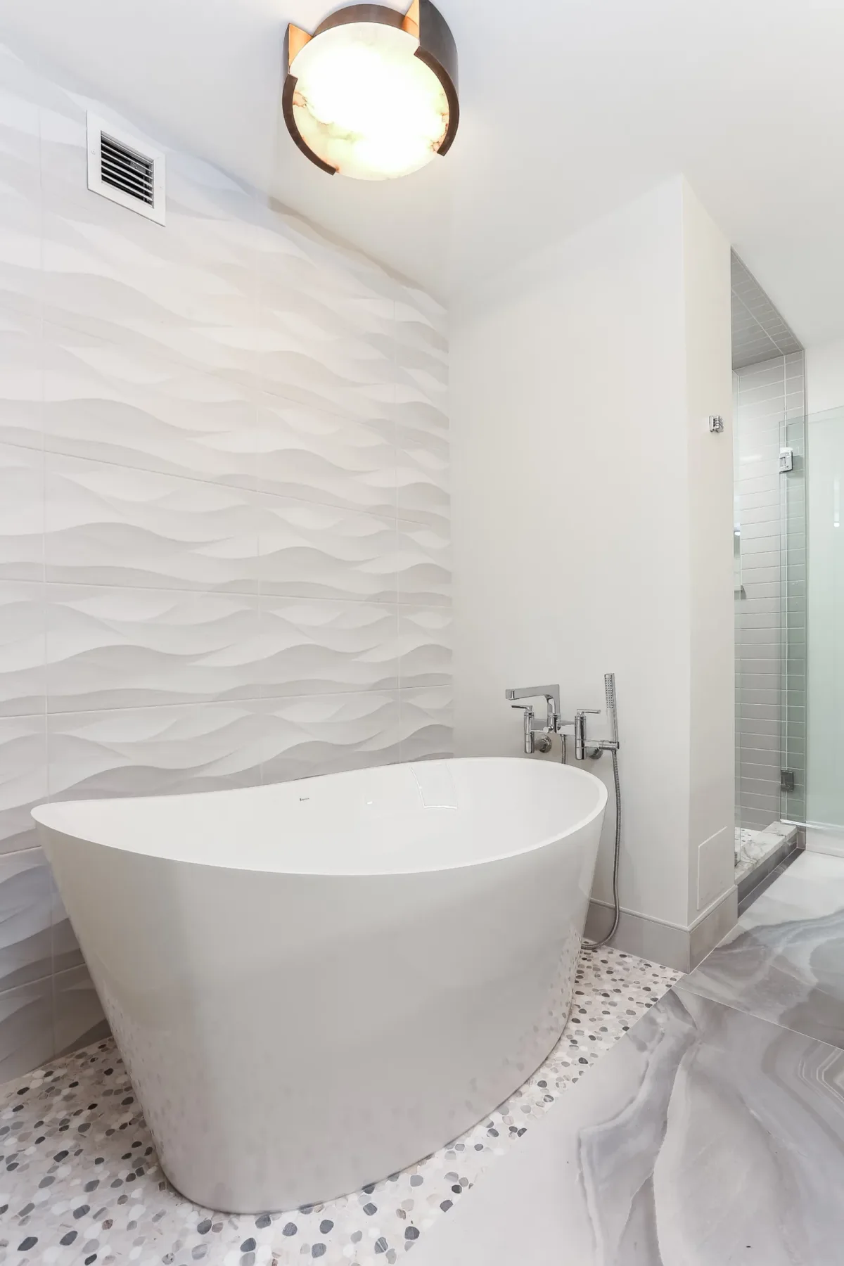 Freestanding tub set against a wave-relief tile wall, condo renovation in Chicago, IL