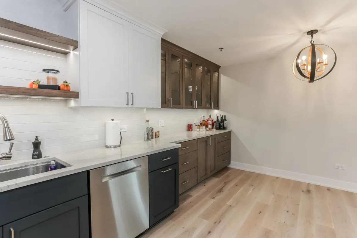 Glass-front upper cabinets with lit interiors over a stained lower cabinet run in a Chicago condo kitchen renovation