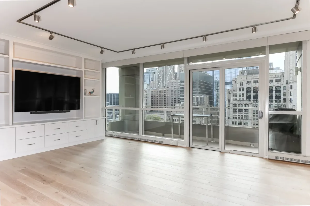 White built-in media wall and shelving in a Chicago condo renovation living room, opposite a wall of glass