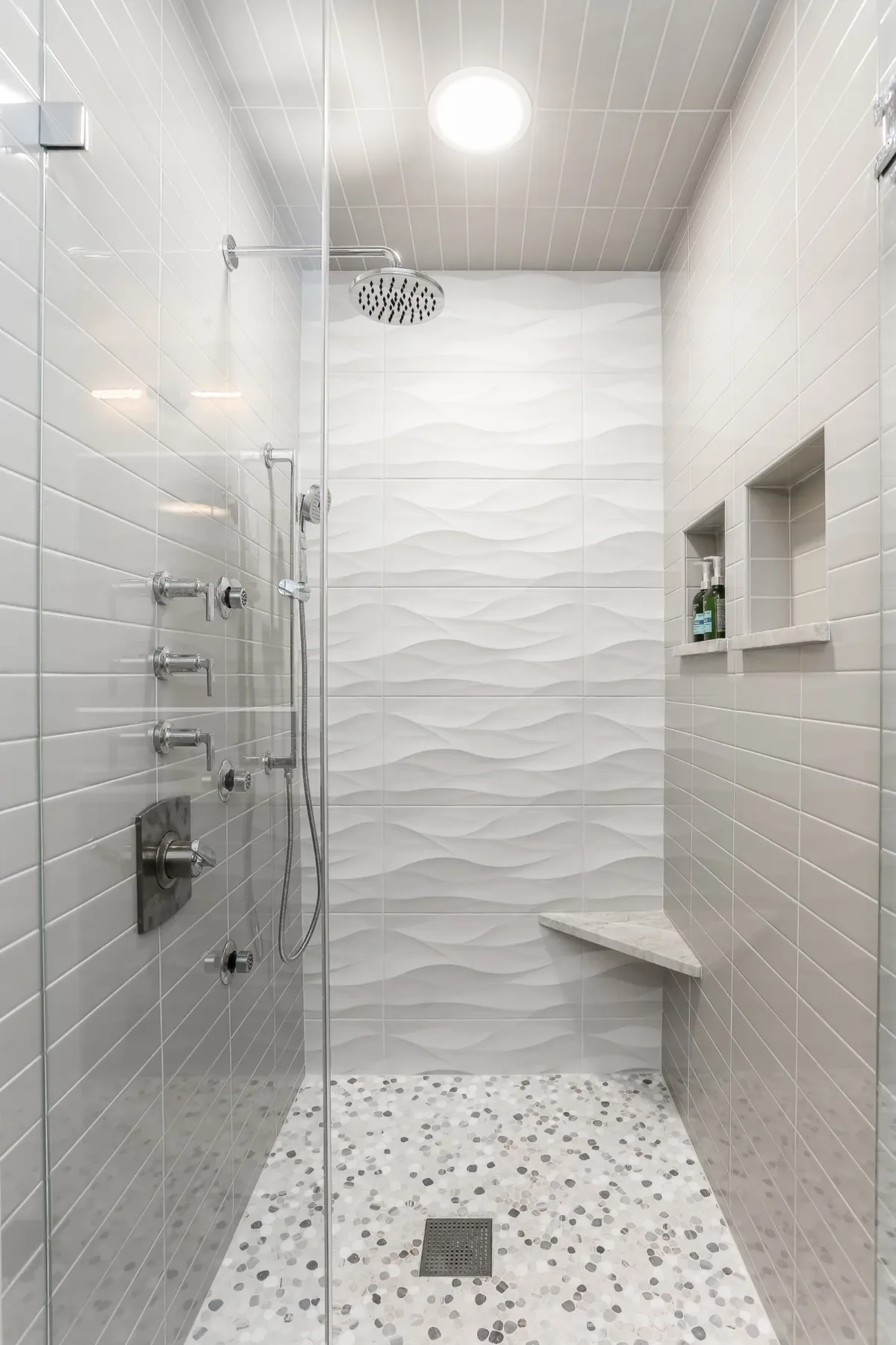 Frameless glass shower with rain head, hand shower and body sprays over a pebble mosaic floor in a Chicago condo bathroom renovation