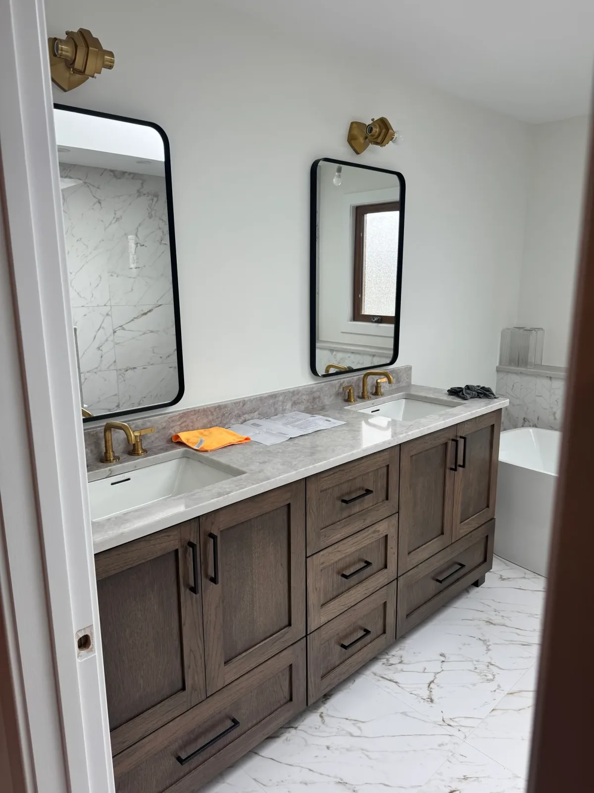 Bathroom remodel after photo, Mokena IL - stained oak double vanity with a marble top, rectangular undermount basins, black-framed arch mirrors and brass tapware