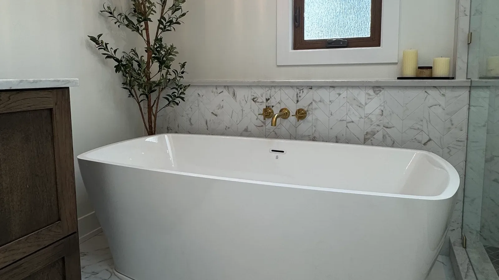 Marble primary bathroom remodel in Mokena, IL - freestanding soaking tub against a marble wall with a floor-mounted brass filler by Luxe Development
