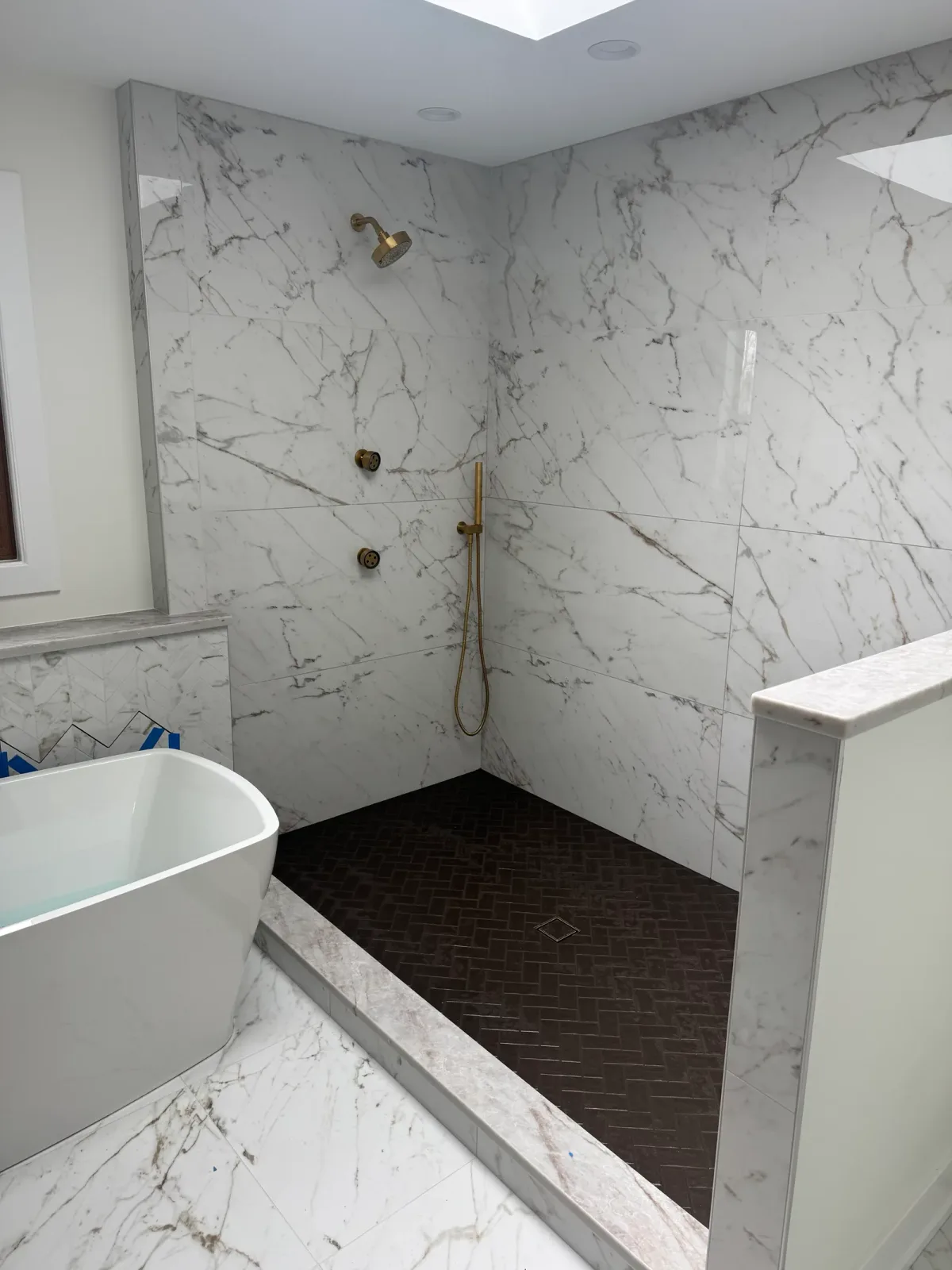Walk-in shower lined in large-format marble with brass thermostatic controls and a brass handshower on a slide bar - marble primary bath remodel, Mokena IL