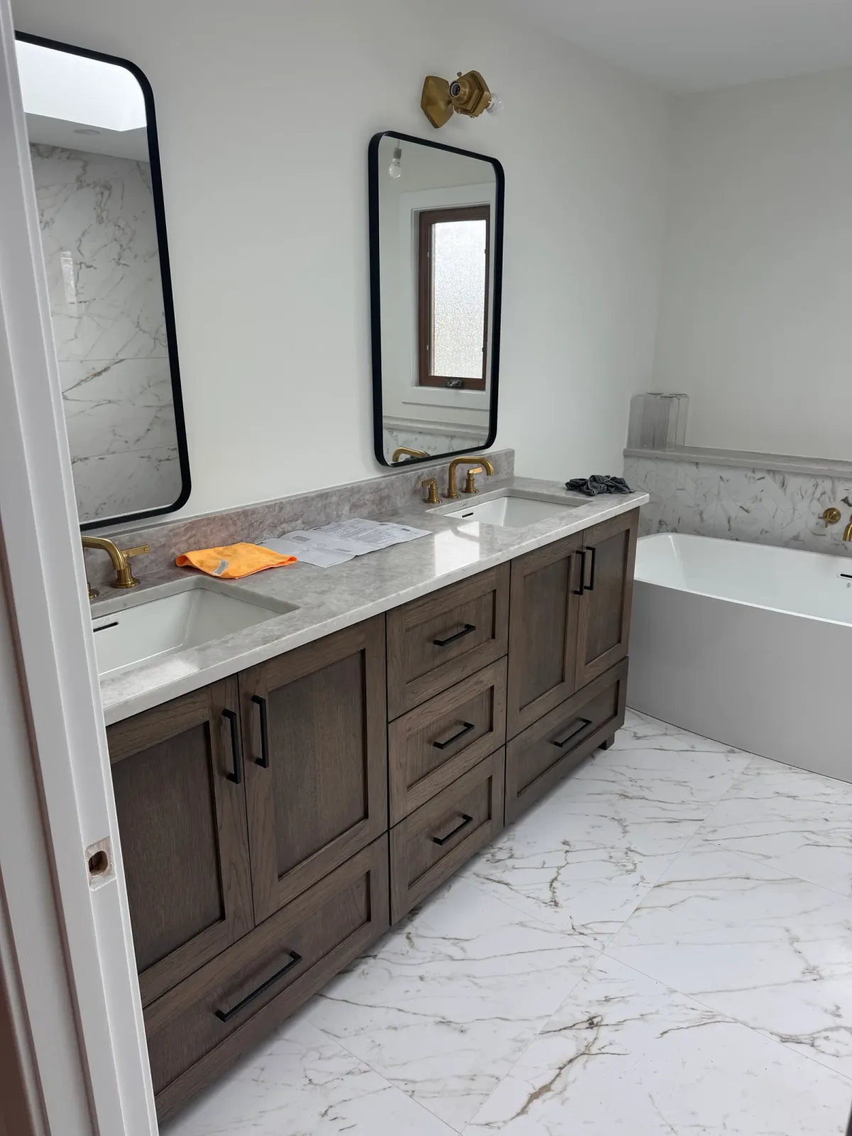Stained oak double vanity with a marble top, two black-framed arch mirrors and brass tapware, with the freestanding tub at the right - marble primary bath remodel, Mokena IL