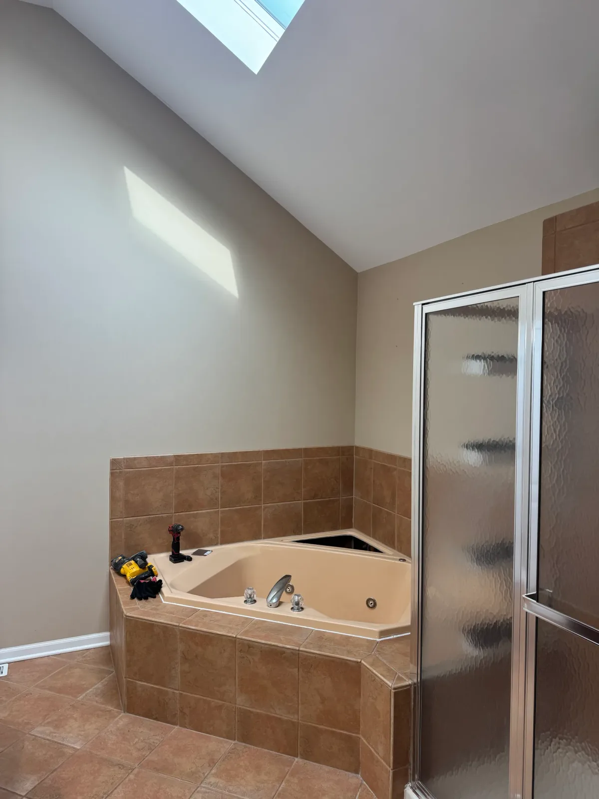 Bathroom remodel before photo, Mokena IL - corner tub set into beige tile beside a framed obscure-glass shower enclosure