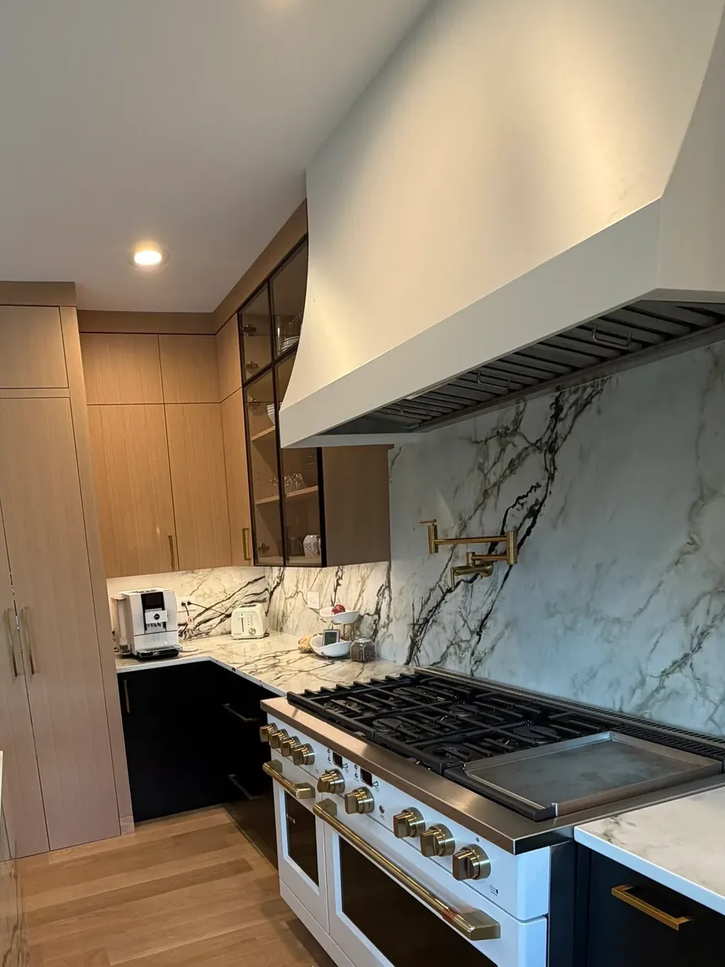 Kitchen range wall with a white professional range on brass knobs and handles, a full-height heavily veined stone backsplash, a brass pot filler and a white hood surround - whole-home renovation, Mokena IL