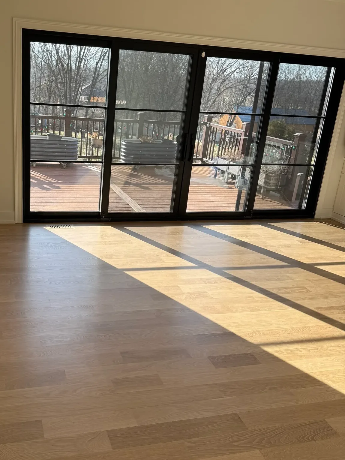 Four-panel black-framed sliding glass door wall opening onto a deck, with low winter light falling in bars across a white oak plank floor - whole-home renovation, Mokena IL
