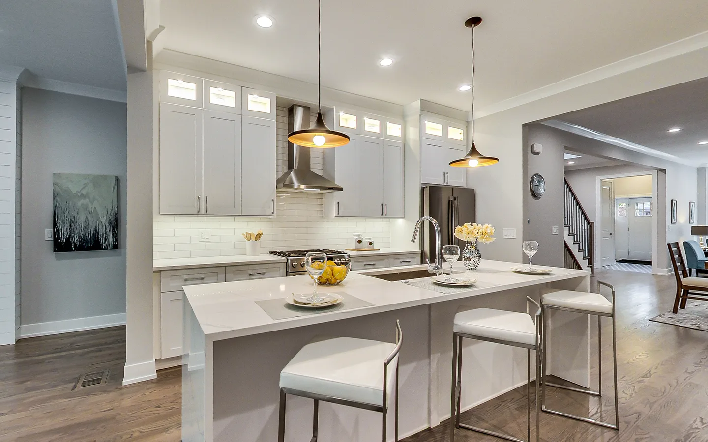 Open-plan white kitchen with a large quartz island and bar seating by Luxe Development