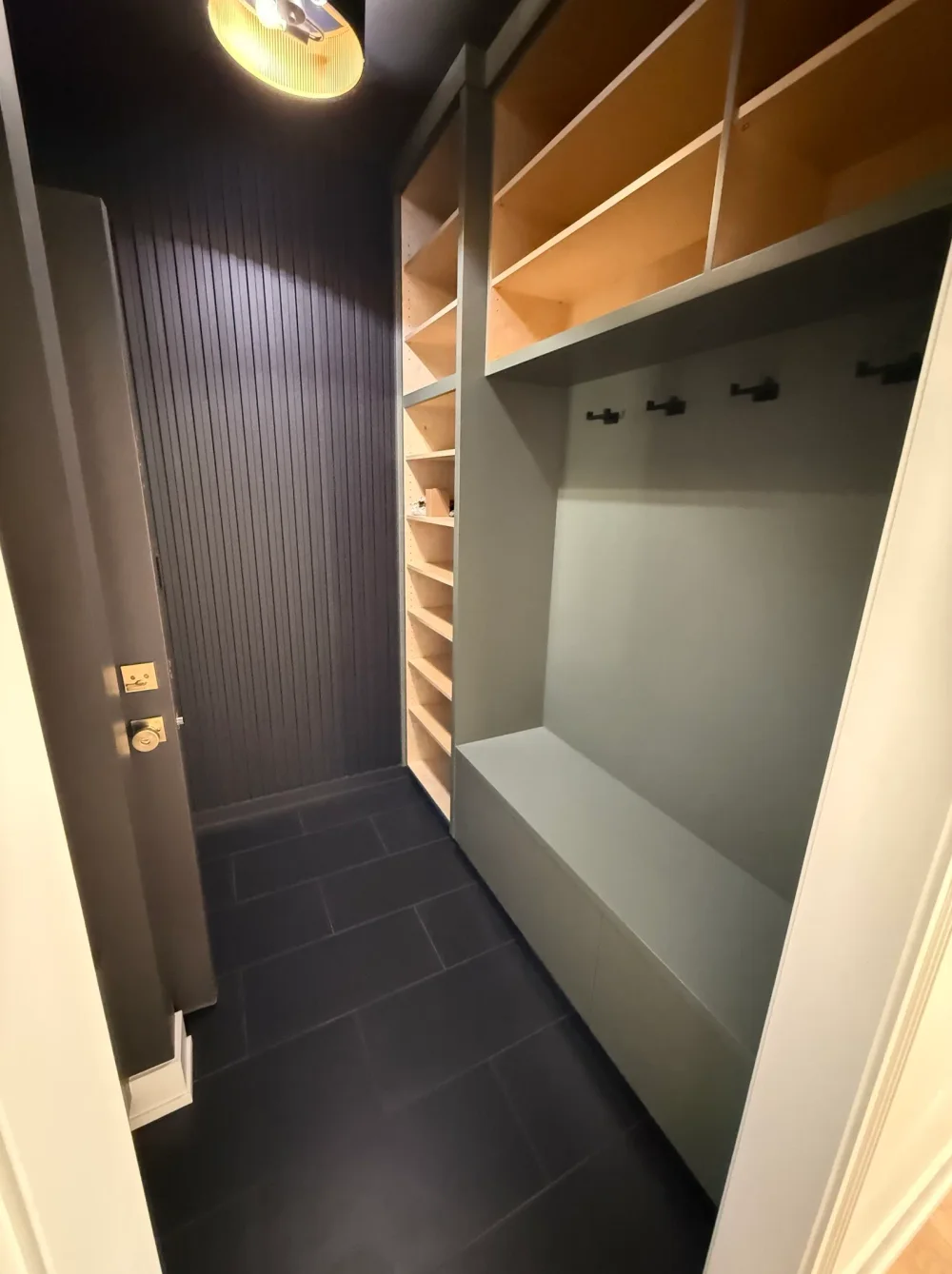 Custom mudroom built-ins with a painted bench, black coat hooks and natural-wood cubby shelving from a whole-home renovation